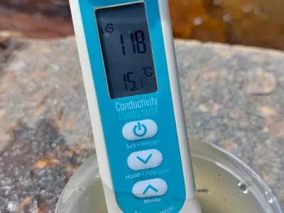 A handheld conductivity meter in a water sample.